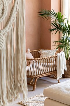 Macrame wall hanging frames a low rattan crib with soft textiles against warm terracotta walls in a boho-inspired nursery setting