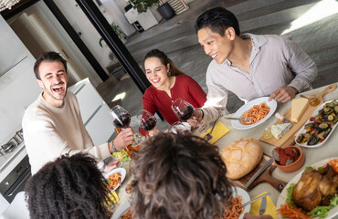 Fototapeta premium Raised wine glasses and broad smiles capture a spontaneous toast among young friends over lunch. The multicultural gathering celebrates connection, inclusion and the joy of sharing food.