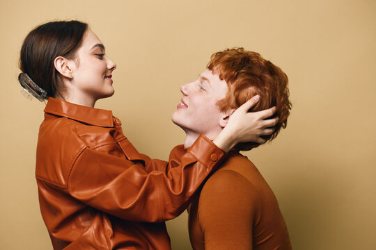 Couple, woman and man with love and affection in warm clothing on brown background. Young people embracing, smiling and looking at each other with happiness and connection.