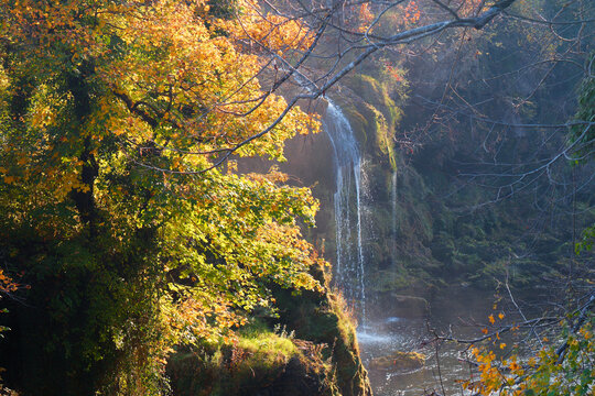 Cascading waterfalls pour over mossy rock terraces into the emerald Slunjčica River, surrounded by vibrant autumn foliage in the picturesque village of Rastoke, Slunj.