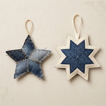 Two decorative fabric star ornaments featuring a rustic denim patchwork design and a geometric quilted pattern with cream borders, hanging on a neutral surface