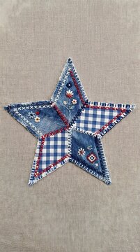 Handmade fabric star ornament made from denim and blue gingham patches with decorative embroidery stitching on a textured rustic background