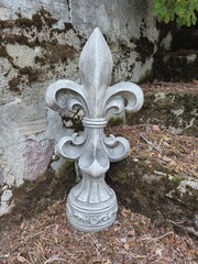 Stone fleur de lis garden ornament standing on mossy background outdoors © Оксана Жемеренко
