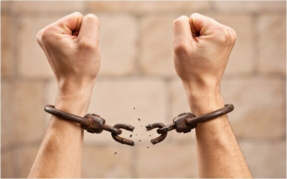 Human hands with broken iron shackles, raised fists against a brick wall
