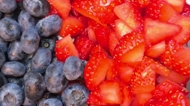 Fresh blueberries and sliced strawberries close up. Ripe berries background with red and blue fruits. Healthy food, summer harvest and natural vitamin dessert concept