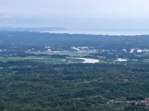 Aerial view of the Cox's Bazar 60 MW US-DK Wind Power Plant situated amidst lush green landscape, winding river, and distant coastline in Cox's Bazar, Chittagong Division, Bangladesh.