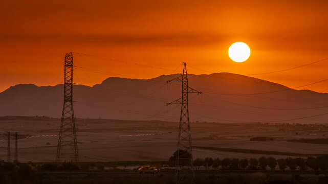 Murcia, Spain- 15th September 2024 - High Voltage Electricity Pylons Silhouetted Against Vivid Orange Sunset Sky Over Rural Mountain Landscape