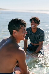 Fototapeta premium Smiling young men in shallow sea laughing together summer portrait for social media banner and promotional background