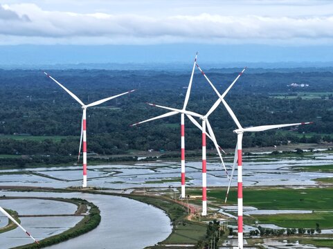 Aerial view of Cox's Bazar 60 MW US-DK Wind Power Plant with red and white turbines in a flooded landscape with green fields and a river in Cox's Bazar, Chittagong Division, Bangladesh.