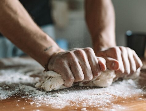 Close-up view of a chef's hands kneading fresh bread dough on a flour-dusted worktop. 