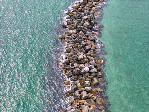 Aerial view of The Jetty at the South End of Wrightsville, a stone breakwater separating turquoise ocean waters in Wrightsville Beach, North Carolina, United States.