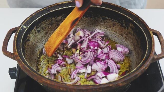Sliced red onions are fried in vegetable oil in a deep cast-iron skillet