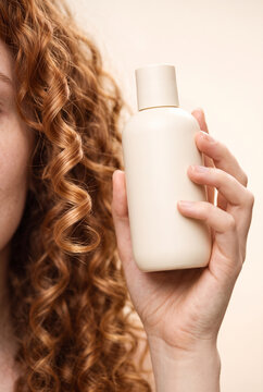 Woman holding a shampoo bottle with curly hair in a neutral setting  