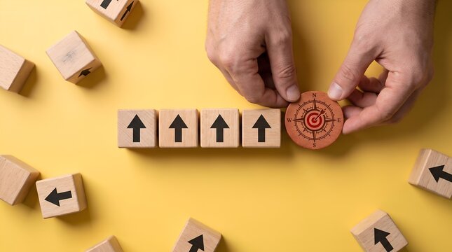 Hand placing wooden compass on row of wooden blocks with arrows