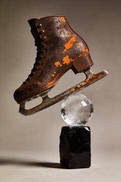 An old brown leather ice skate with a rusty blade balanced on a clear glass sphere and black stone pedestal. Creative ice skates blade rust concept.