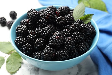 Many fresh blackberries and green leaves in bowl on light marble table, closeup © New Africa