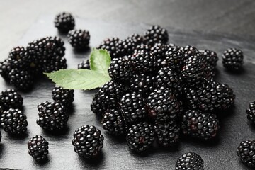 Pile of fresh blackberries and green leaves on dark textured table, closeup © New Africa