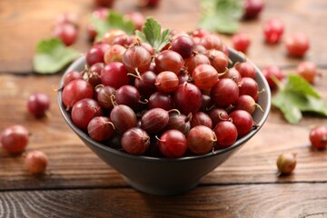 Fresh red gooseberries in bowl and green leaves on wooden table, closeup © New Africa