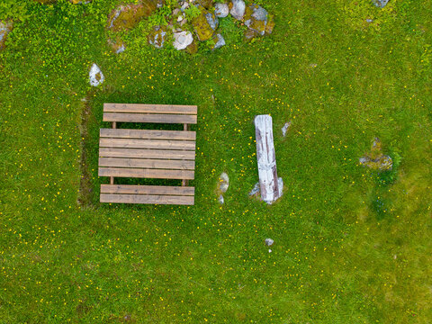 Aerial view of a wooden picnic table and a bench set on a lush green meadow dotted with yellow wildflowers and scattered stones in Sylte, More og Romsdal, Norway.