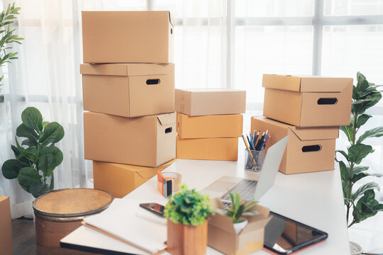 Moving Boxes and Workspace: A clutter of cardboard boxes is stacked around a desk with a laptop and office supplies, suggesting a relocation or organization project.