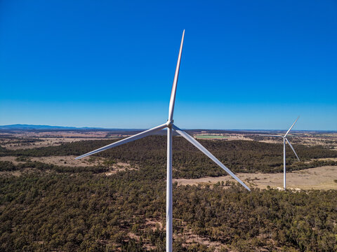 Aerial view of wind turbines standing in a rural landscape with green and brown vegetation under a clear blue sky in Diamondy, Queensland, Australia.