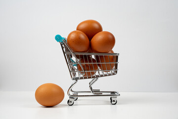 Miniature shopping cart filled with brown eggs, symbolizing high food prices and consumer spending on essential groceries © Alberto
