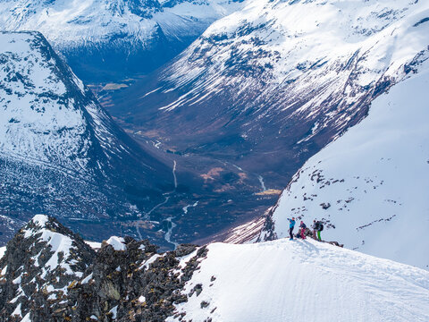Aerial view of Ringshornet mountain ridge with hikers standing on the snow-covered peak overlooking a deep valley in Fjord, More og Romsdal, Norway.