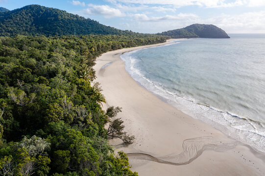 Aerial view of Cape Tribulation beach where the Daintree Rainforest meets the ocean, featuring white sand, dense tropical vegetation, and turquoise waves in Daintree, Queensland, Australia.