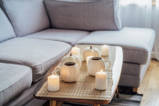 Autumn fall mood composition for hygge home decor. Hot tea or coffee drink in pumpkin's shaped cups, pumpkin decor and burning candles on the coffee table. Festive autumn, fall mood home decor