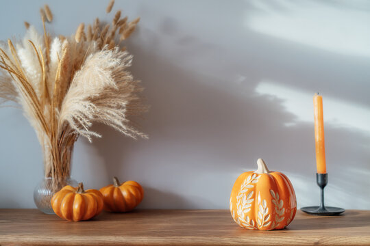 Cozy warm autumn home interior - decorative orange ceramic pumpkins, candles, dried flowers on the wooden console with white wall background. Scandinavian minimalist hygge home fall decor