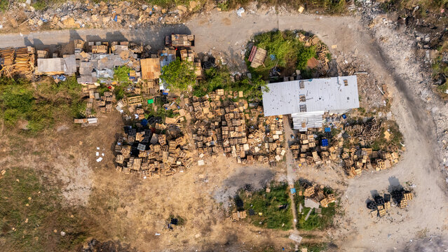 Aerial view of a storage area filled with numerous stacked wooden pallets, a small industrial building, and dirt ground in Central Java, Indonesia.