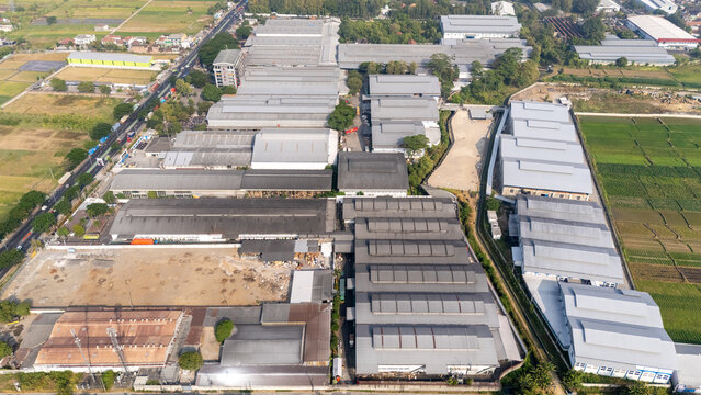 Aerial view of a large industrial factory complex with multiple metal-roofed warehouses, adjacent to green agricultural fields and a road in Central Java, Indonesia.