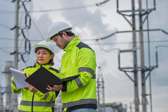 Male and female engineers review technical data using a laptop and documents at an electrical power facility. Concept of power generation, inspection, energy infrastructure, teamwork, and engineering.