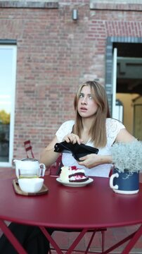 Vertical screen student discovers that money was stolen at a cafe as she checks her empty wallet with a shocked worried expression and realizes she cannot pay for her dessert

