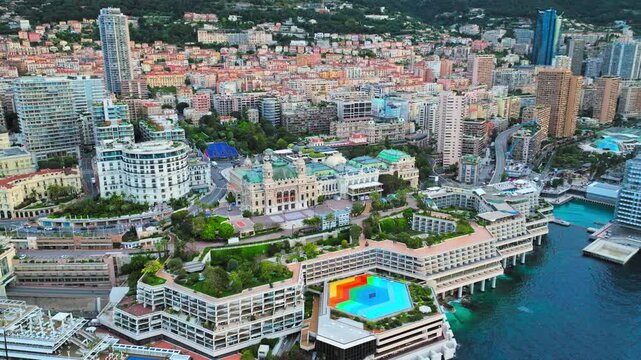 Drone view of Monaco waterfront and Port Hercules. Curved harbour walls, city buildings, yachts and blue sea create a scenic luxury coastal panorama.