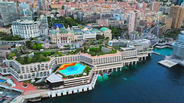Drone view of Monaco waterfront and harbour. Curved marina walls, luxury buildings, yachts and blue Mediterranean water create a scenic Riviera cityscape.