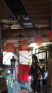 Marrakech, morocco. August 9, 2026. Narrow alley in a traditional moroccan market in marrakech, decorated with national flags. A person wearing a djellaba walks in the background