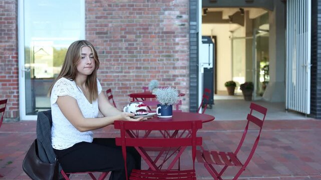 Woman holds a slice of cake at outdoor cafe but hesitates to eat it struggling between dessert cravings and her desire to lose weight while practicing strong self control
