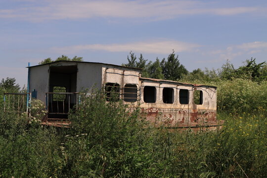 An old metal river boat with traces of rust and peeling paint standing in tall grass under a clear summer sky. The concept of the passage of time, decay and urbex.