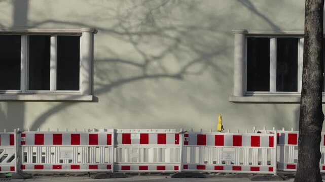 Red and white construction barriers blocking sidewalk in Munich, Germany. Ongoing urban reconstruction and constant repair works causing inconvenience, typical infrastructure maintenance.