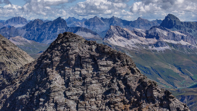 Aerial view of the rugged rocky peaks of the Alps near Madesimo, featuring dramatic mountain ridges and deep valleys under a blue sky in Madesimo, Lombardie, Italy.