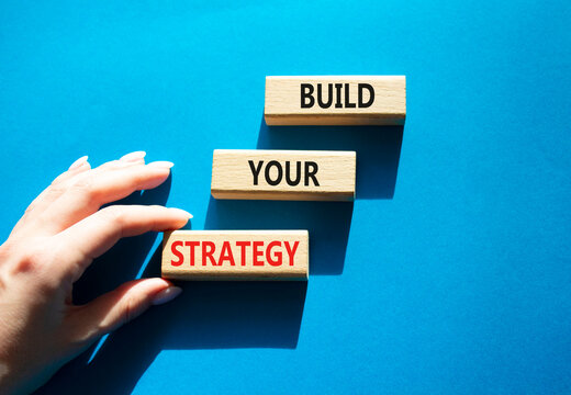 Build your strategy symbol. Concept words build your strategy on wooden blocks arranged as steps. Businessman hand near wooden blocks. Strategic planning concept. Blue background. Copy space.