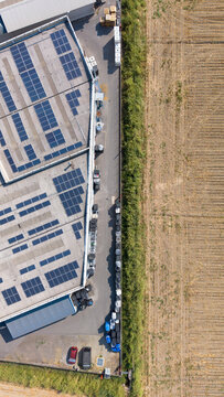 Aerial view of a paint manufacturing facility featuring extensive rooftop solar panels, adjacent to agricultural fields in Milan, Lombardy, Italy.