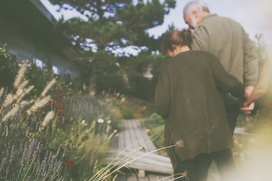 Elderly couple walking hand in hand down a weathered garden path, a serene and devoted scene with muted tones for retirement living and later-life care