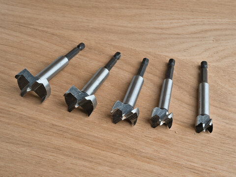 Five Forstner Drill Bits on Wood Surface - Set of five steel Forstner drill bits arranged on a light oak wooden surface, varying sizes for woodworking.