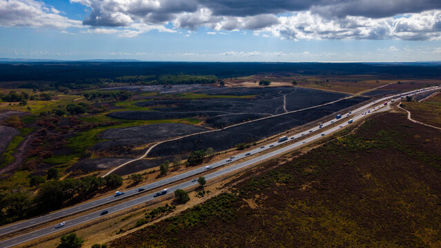 Aerial view of the A31 road passing through New Forest National Park, showing a wildfire burn scar on the landscape with vehicles traveling in New Forest District, England, United Kingdom.