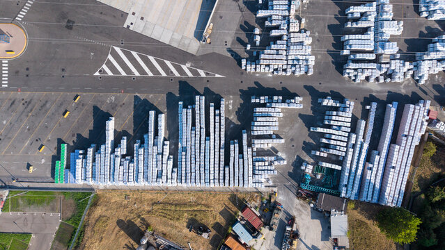 Aerial view of an industrial manufacturing facility with rows of stacked white building material bags and production infrastructure in Peschiera Borromeo, Lombardy, Italy.