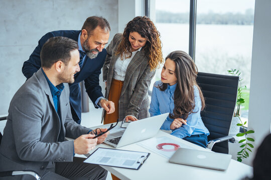 Business Team Meeting Around Laptop Collaborating On Project Strategy In Modern Office