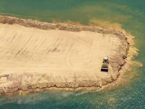 Aerial view of a bulldozer working on a sandy construction site along the coastline in Piraeus, Greece.