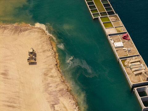 Aerial view of a bulldozer working on a dirt embankment next to industrial concrete structures in the water at the port of Piraeus, Greece.